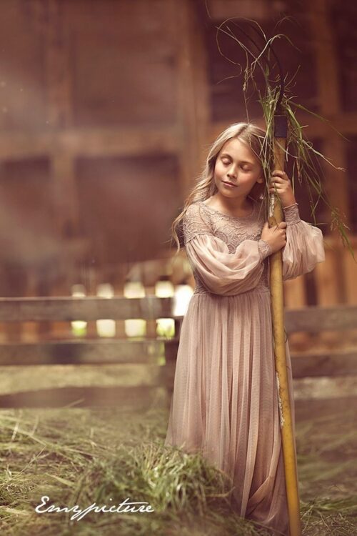 Child wearing a boho style lace dress standing in a rustic barn interior