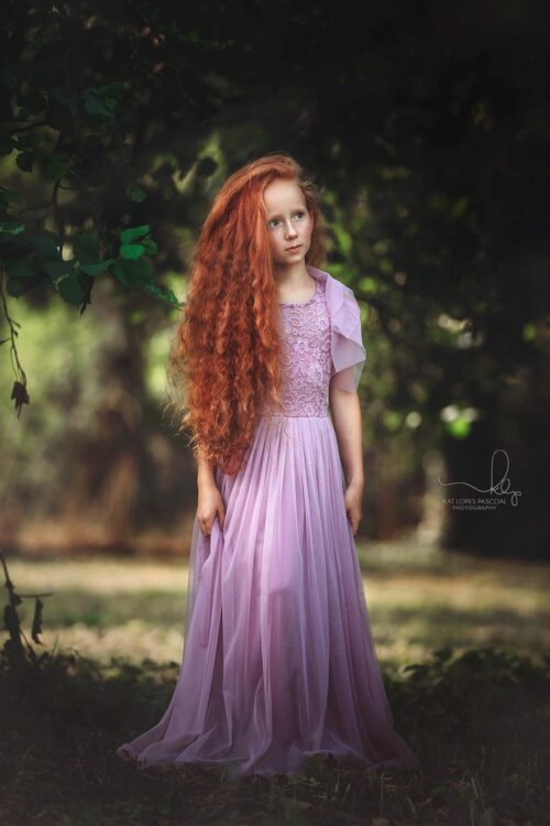 Girl wearing a lace and tulle dress standing in a forest clearing
