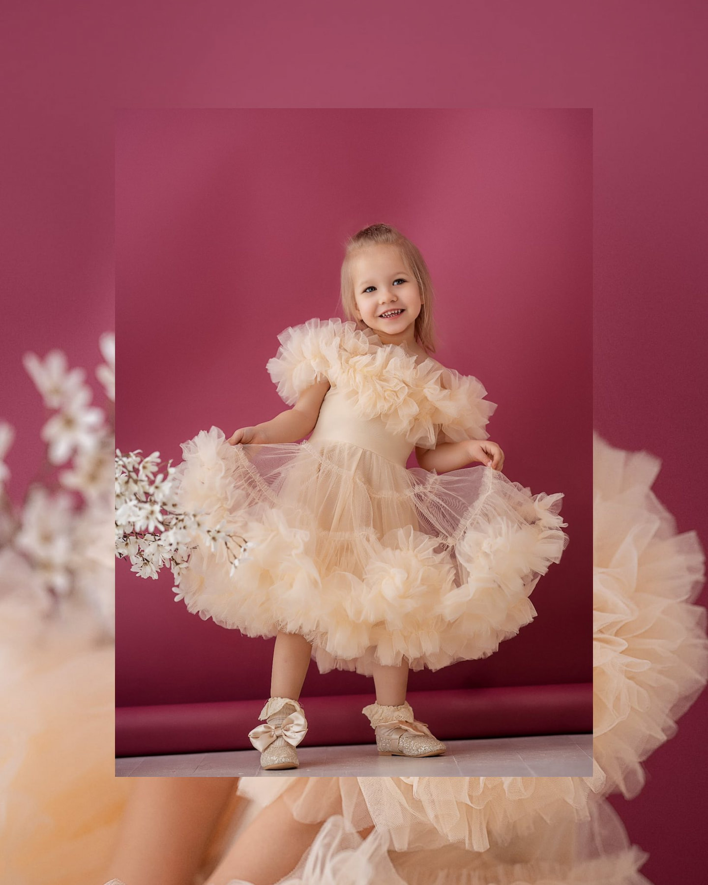 Child in a fluffy tulle dress smiling against a pink background