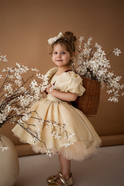 Toddler girl wearing an elegant gold dress with puff sleeves and floral branches