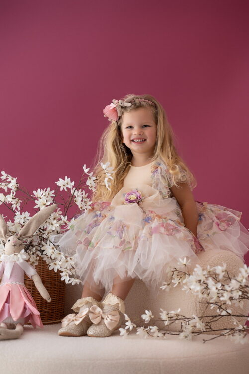 Toddler girl wearing a floral tulle dress sitting in a studio with flowers