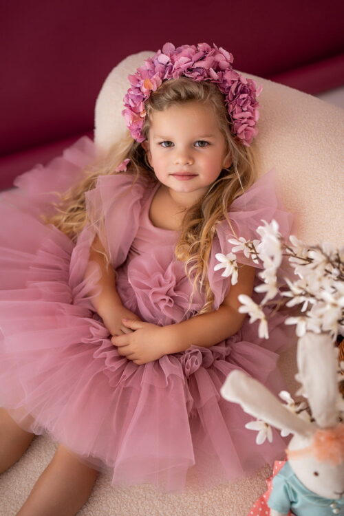 Toddler girl wearing a tulle dress with ruffled shoulders sitting in a studio