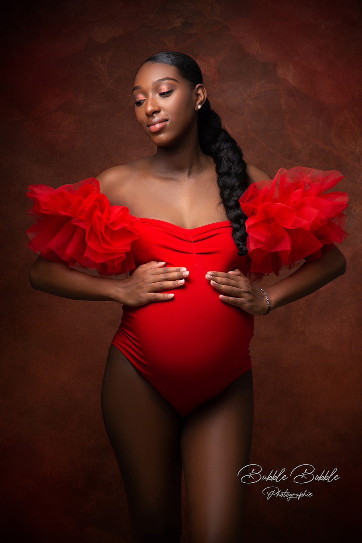 Pregnant woman in red Scarlett bodysuit with dramatic tulle sleeves, artistic maternity portrait