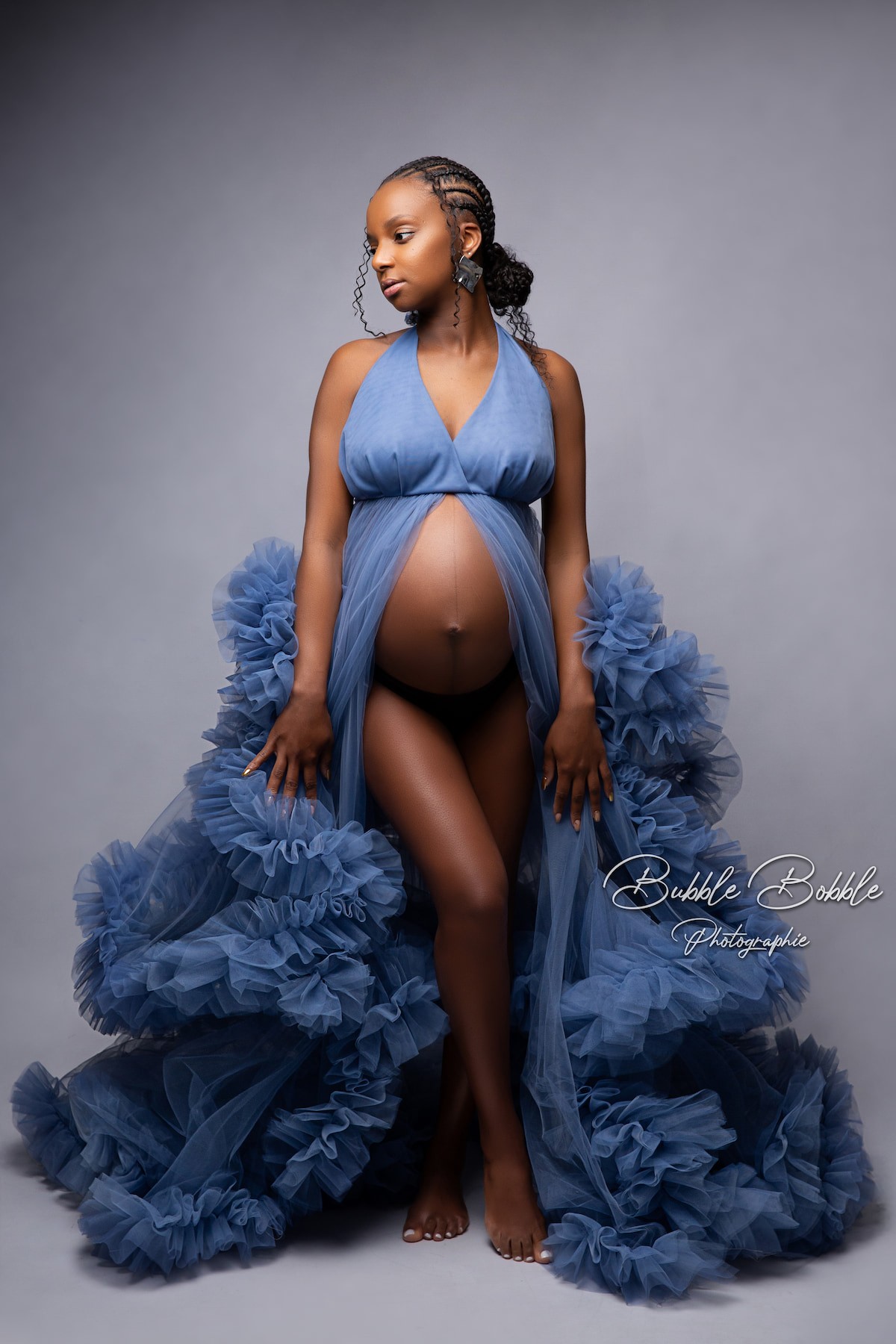 Pregnant model in Rumba tulle gown in denim blue, styled for artistic maternity photoshoot with dramatic layered train.