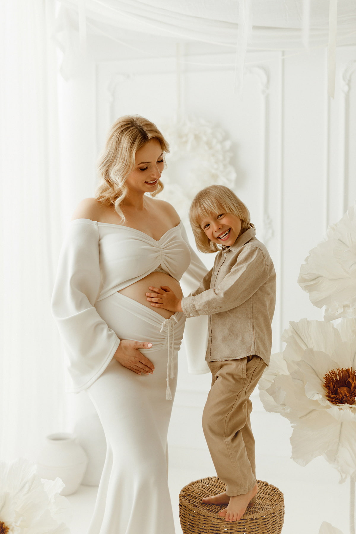 Mother-to-be wearing a white maternity gown with long sleeves while smiling with her child, timeless pregnancy photography dress by Kamaprops.