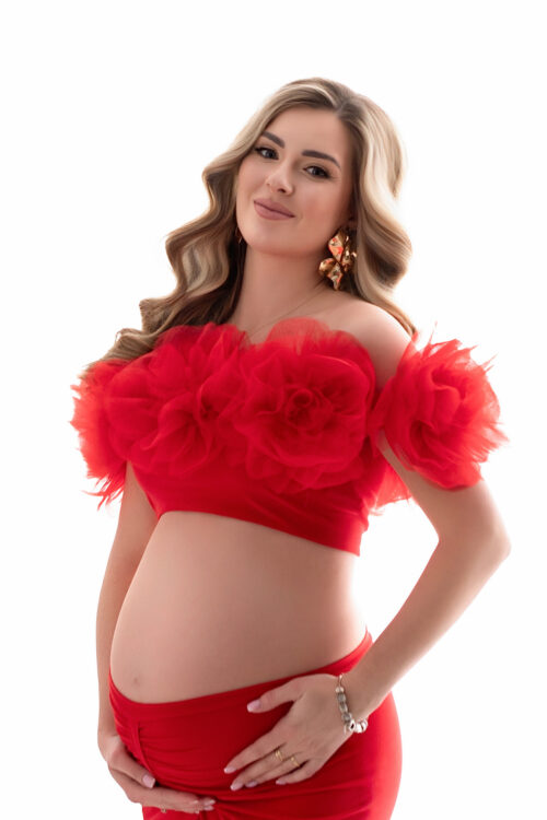 Pregnant woman wearing red maternity outfit with tulle floral shoulder wrap
