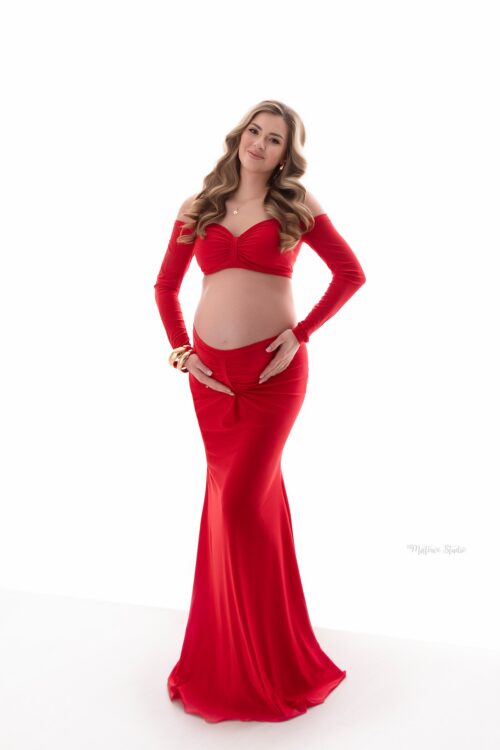 Pregnant woman wearing red off-shoulder maternity set with long sleeve top and ruched maxi skirt