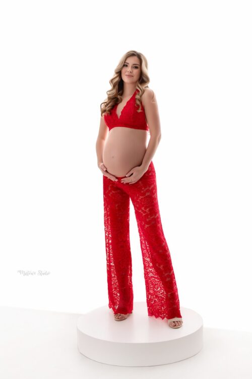 Maternity photoshoot outfit with red lace bralette and transparent loose pants highlighting baby bump