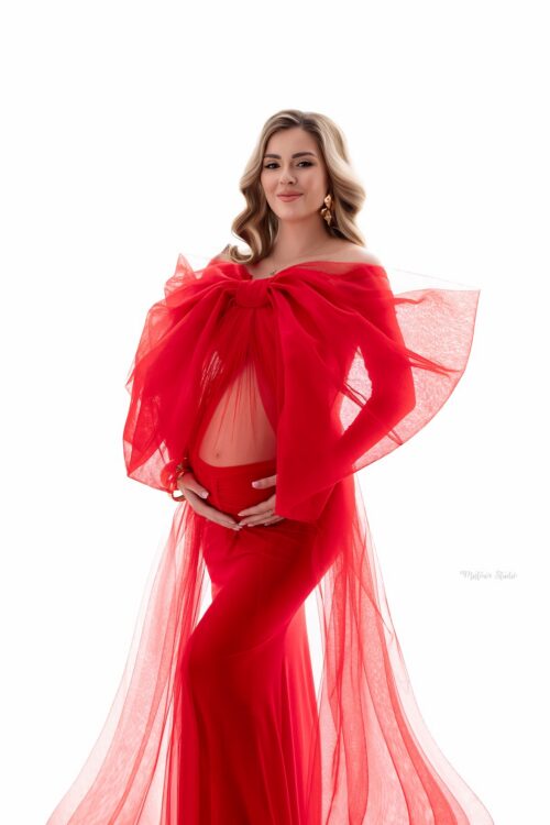 Pregnant woman wearing red maternity gown with dramatic tulle bow veil accessory