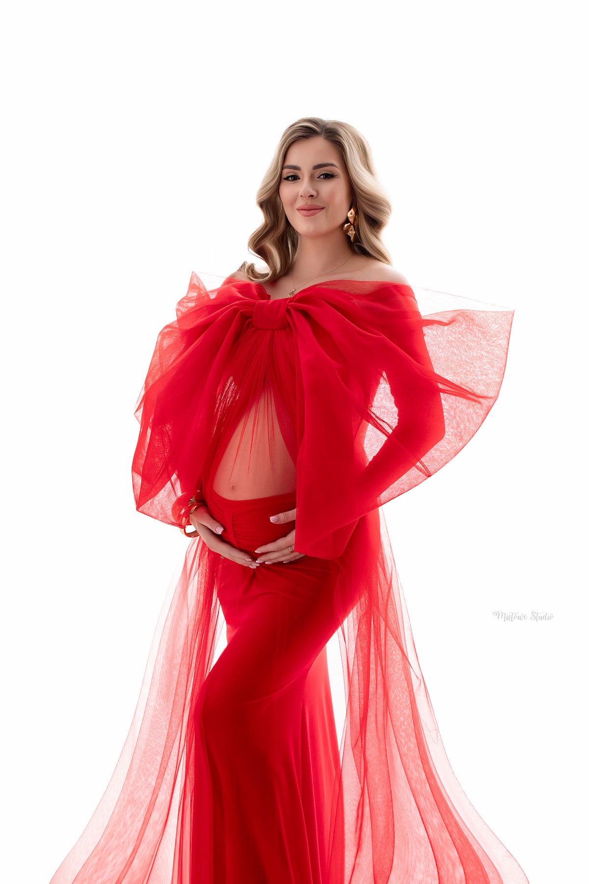 Pregnant woman wearing red maternity gown with dramatic tulle bow veil accessory