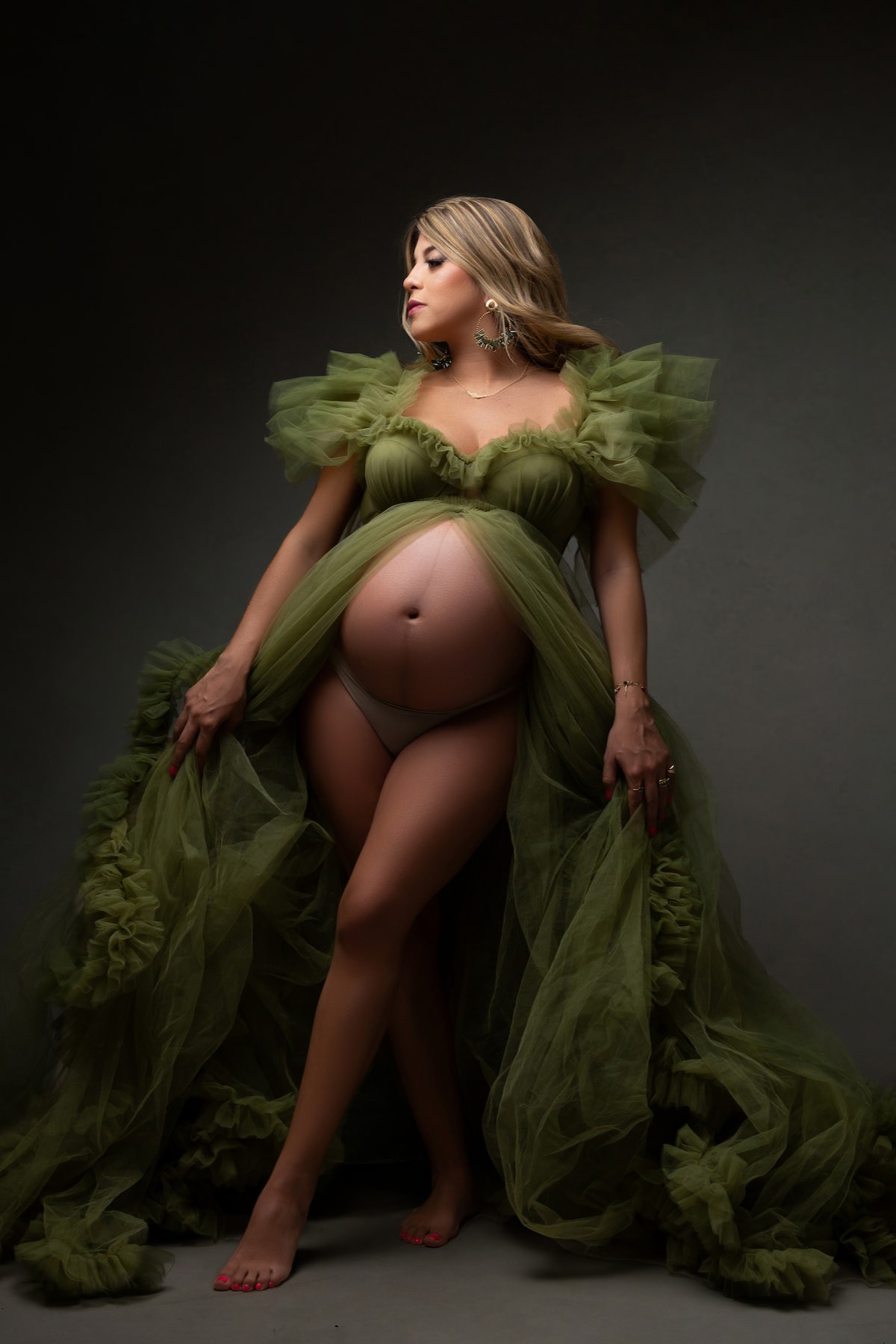 Pregnant woman in olive green Kara dress on dark fine art background